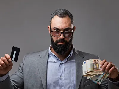 Bărbat bărbos ţinând în mâna dreaptă un card bancar şi în stânga bancnote euro - Foto: Magnific.com/fxquadro