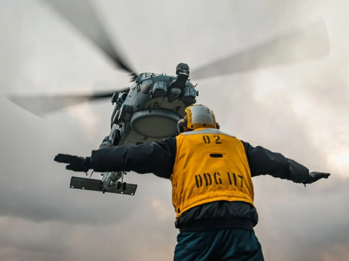 Ironia sorţii - 7.12.2022. Un militar american ghidează un elicopter MH-60R Sea Hawk din Forțele Aeriene Regale Daneze, pentru a ateriza pe puntea distrugătorului american USS Paul Ignatiu - Foto: Profimedia Images