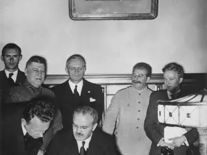 Ministrul sovietic de externe Viaceslav Molotov semnând Pactul Molotov-Ribbentrop. În spatele său, în picioare, la stânga, se află ministrul german de externe Joachim von Ribbentrop și, în dreapta, premierul sovietic Iosif Visarionovici Stalin