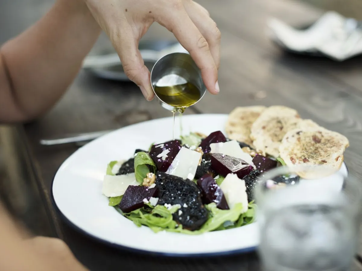 O femeie garniseşte salata cu ulei de măsline - Foto: Magnific.com/Rawpixel.com