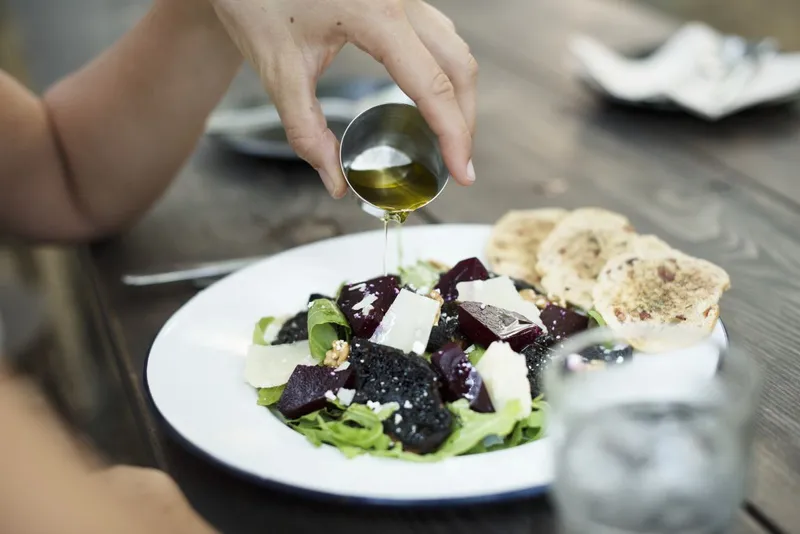 O femeie garniseşte salata cu ulei de măsline - Foto: Magnific.com/Rawpixel.com