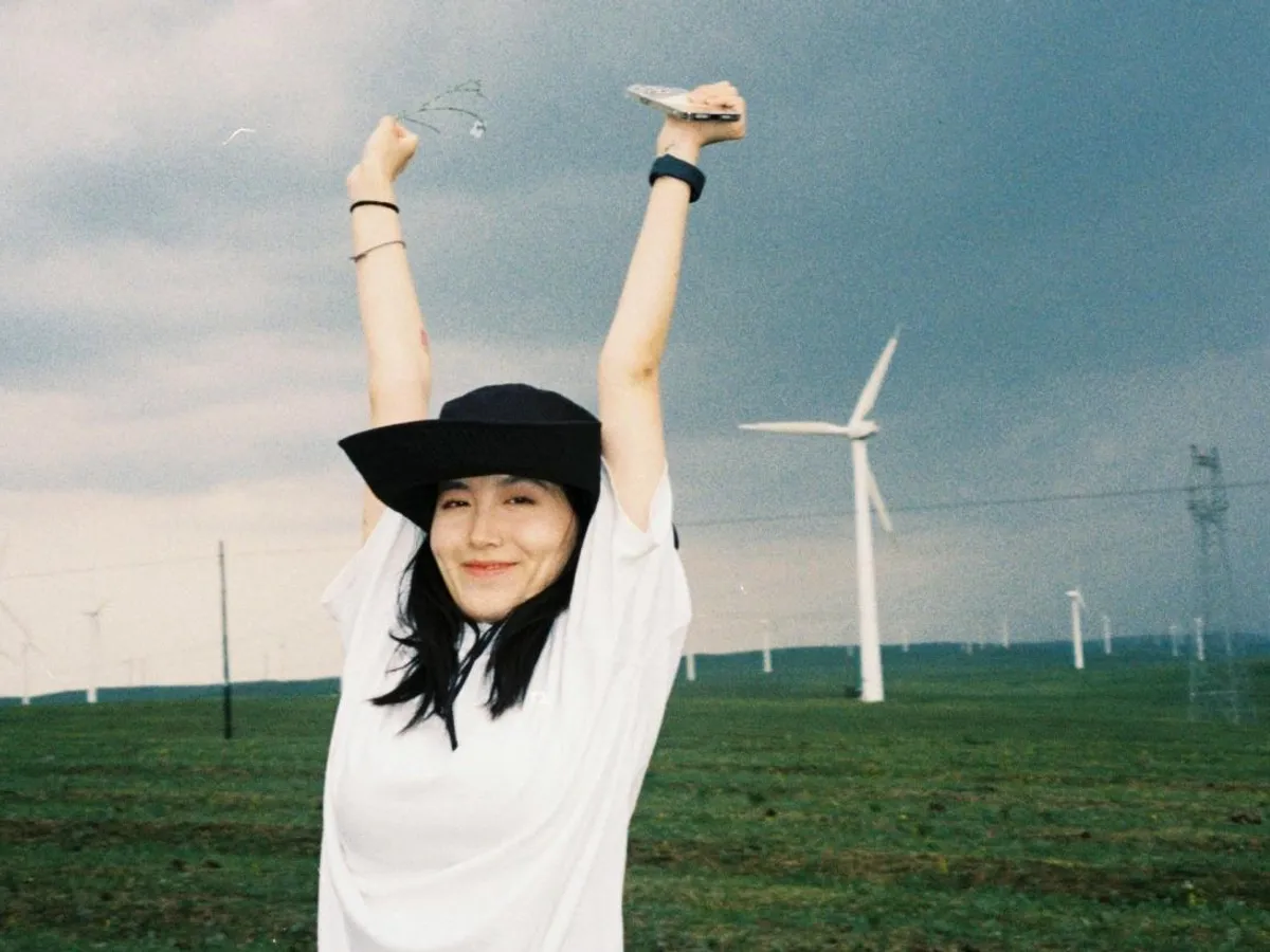 Femeie veselă cu fundal cu mori eoliene - Foto: Pexels/yating yang