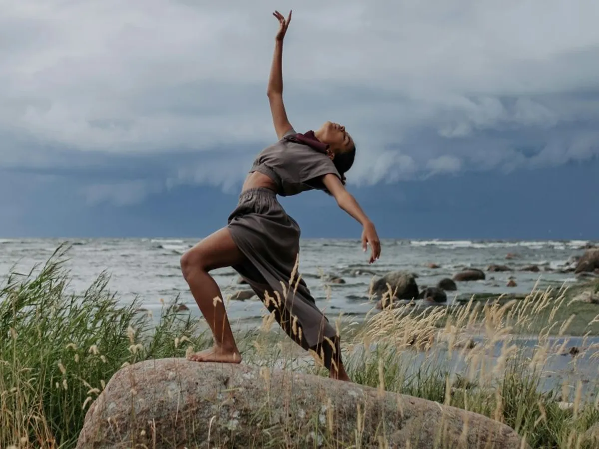 Femeie în robă gri dansând pe o rocă, pe malul mării - Foto: Pexels/cottonbro studio
