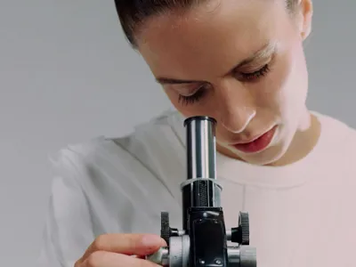 Cercetătoare analizând prin microscop o probă - Foto: Pexels/Ron Lach