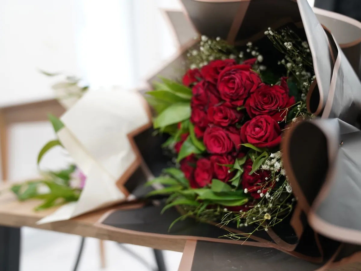 Un buchet frumos de trandafiri roșii aranjați elegant cu verdeață pe o masă de lemn - Foto: Pexels (Imagine cu rol ilustrativ)