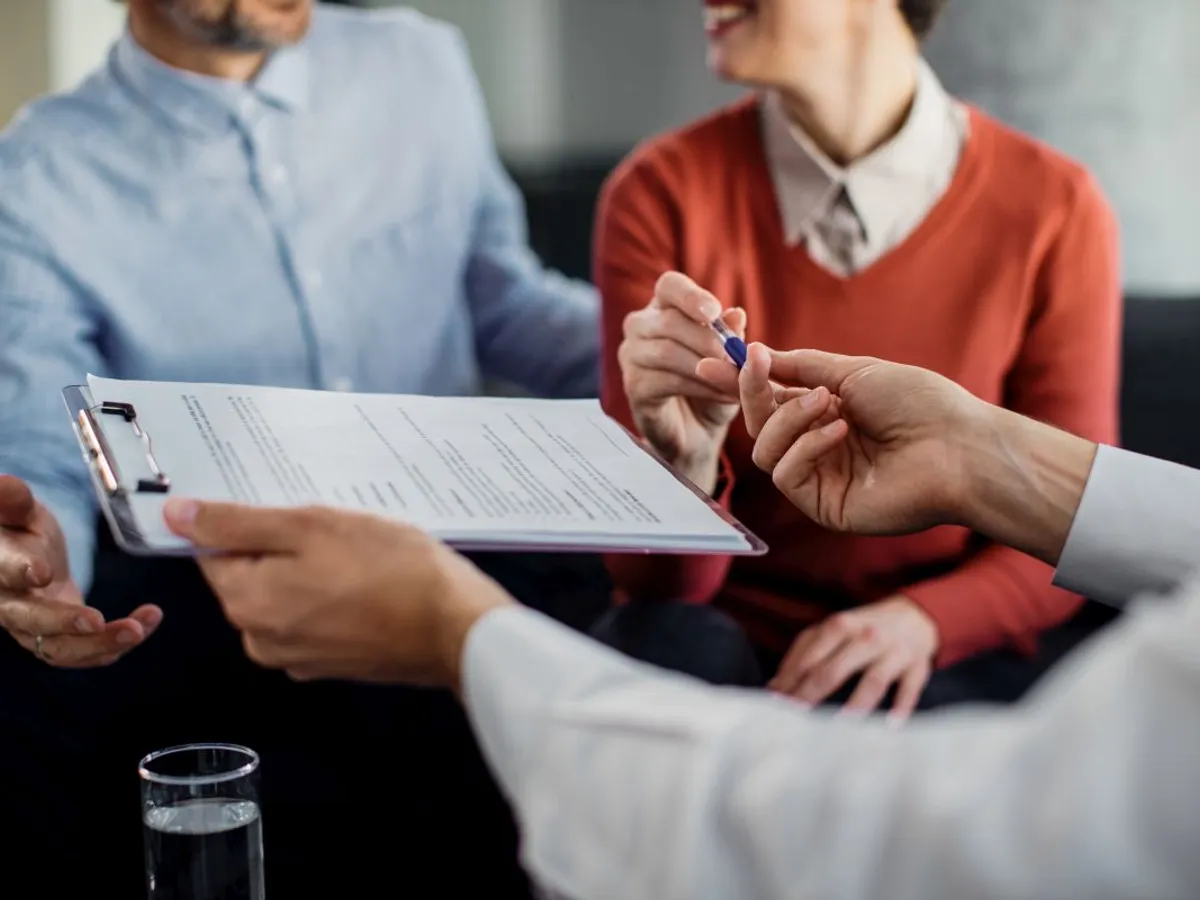 Consultant în asigurări dâ nd asiguratului pixul, pentru a semna contractul - Foto: Magnific.com/Drazen Zigic