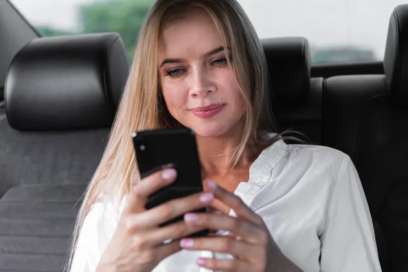 Femeie care verifică telefonul pe bancheta din spate - Foto: Magnific.com (Imagine cu rol ilustrativ)