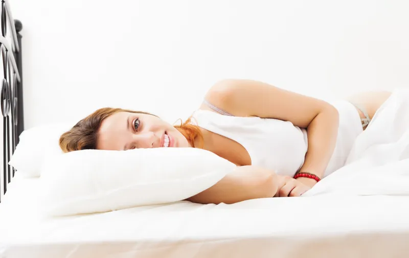 Fată roșcată veselă &icirc;ntinsă pe un cearșaf alb - Foto: Magnific.com (Imagine cu rol ilustrativ)