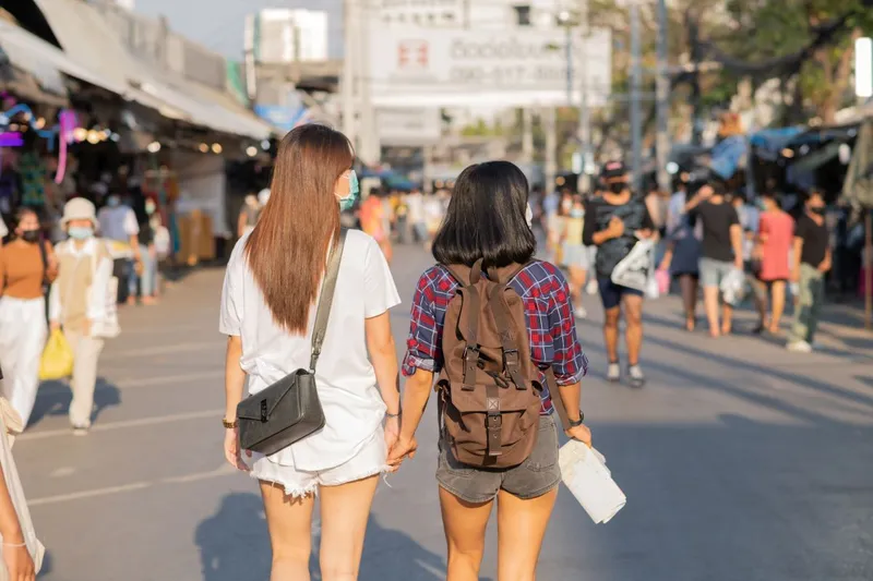 Tinere turiste plimbându-se pe o stradă aglomerată din Thailanda - Foto: Freepik/jcomp