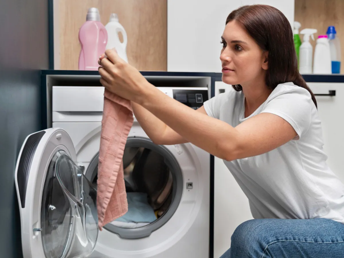 O femeie pune haine în mașina de spălat - Foto: Freepik (rol ilustrativ)