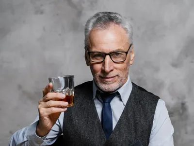 Bărbat elegant în etate ridicând un pahar de whisky - Foto: Freepik/CC0