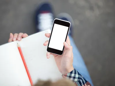 Mână care ține un smartphone pe un caiet cu un creion - Foto: Magnific.com (Imagine cu rol ilustrativ)
