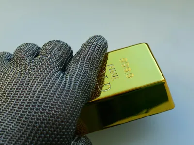 Persoană cu mâna înmănuşată ţinând un lingou de aur - Foto: Pexels/Aurelijus U.