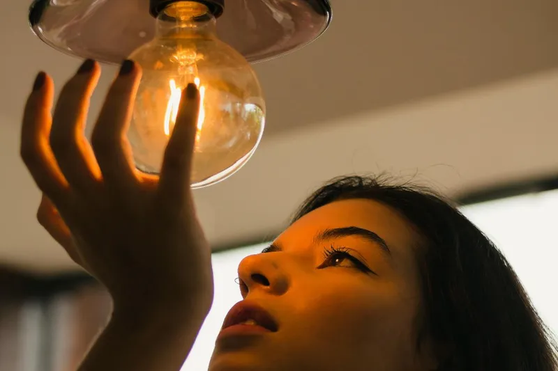 Femeie ţinând în mână un bec cu filament - Foto: Pexels/Luriko Yamaguchi