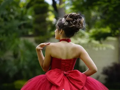 Rochie de ocazie roșie, cu corset și fustă amplă, purtată într-un decor elegant de grădină, ideală pentru nunți, baluri și seri de gală - Foto: Pexels.com