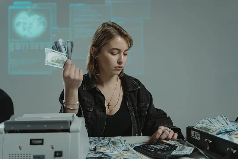 Femeie făc&acirc;nd calcule şi număr&acirc;nd bani, la birou - Foto: Pexels/Tima Miroshnichenko
