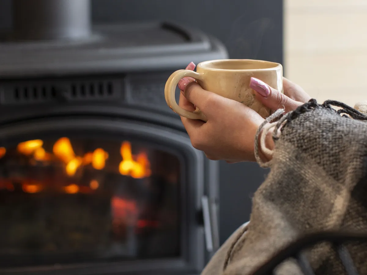 Femeie relaxându-se în faţa şemineului, cu o cană de cafea fierbinte - Foto: Magnific.com/magnific