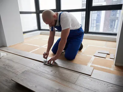 Muncitor de sex masculin desenând linie pe o scândură de lemn laminat într-un apartament - Foto: Megnific.com (Imagine cu rol ilustrativ)