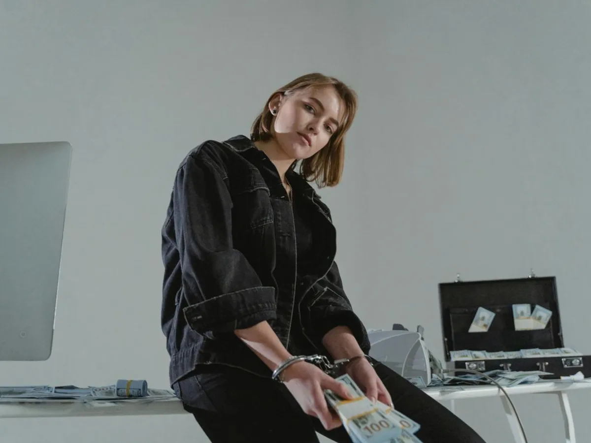 Femeie cu cătuşe la mâini numărând foarte mulţi bani - Foto: Pexels/Tima Miroshnichenko