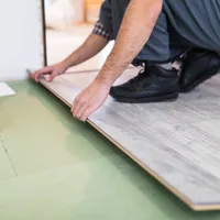 Muncitor care prelucrează o podea cu plăci laminate - Foto: Magnific.com (Imagine cu rol ilustrativ)