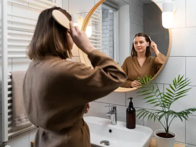 Femeie care se uită în oglindă în baie - Foto: Magnific.com (Imagine cu rol ilustrativ)