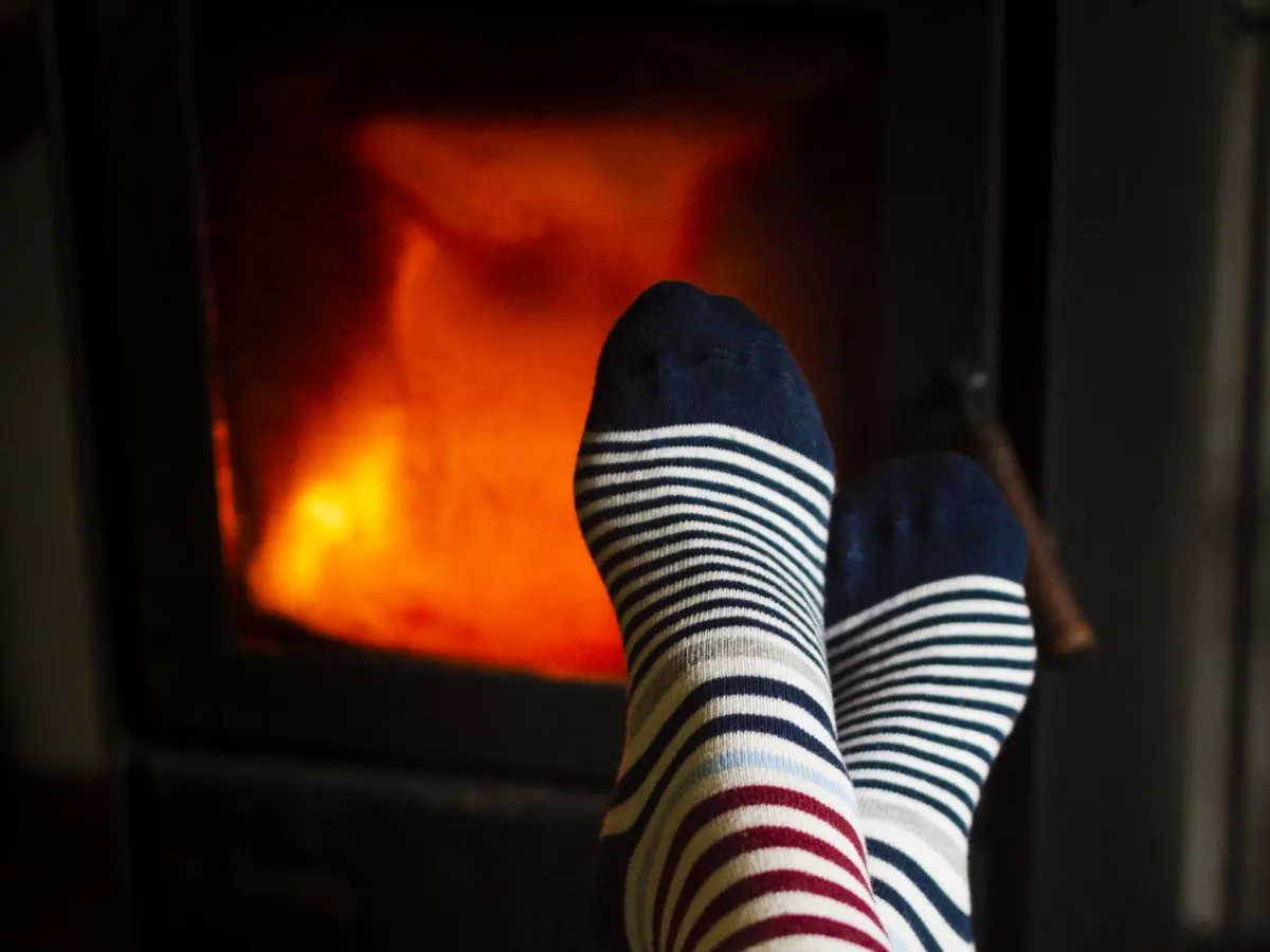 Femeie stând cu picioarele în faţa şemineului cu gaz, la căldură, iarna - Foto: Magnific.com/magnific