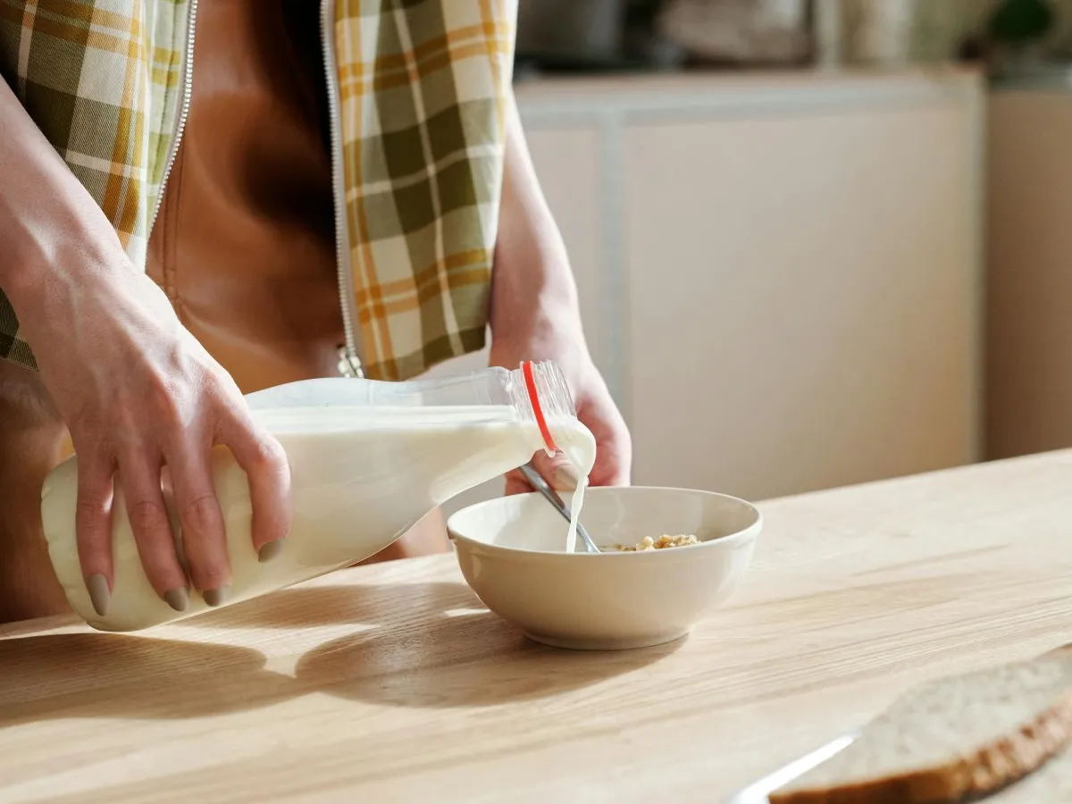 Femeie turnând lapte dintr-o sticlă, într-un bol, în bucătărie - Foto: Pexels/Mikael Blomkvist