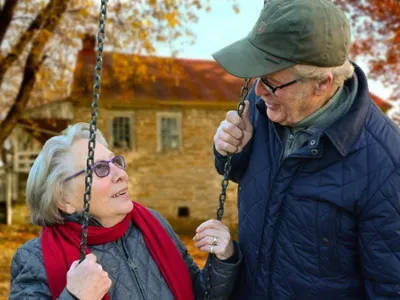 Bărbat în etate stând lângă soţia lui, care se dă într-un leagăn - Foto: Pexels/Pixabay