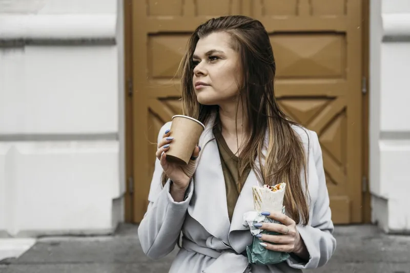 Femeie savur&acirc;ndu-şi cafeaua şi uit&acirc;ndu-se &icirc;n lungul străzii - Foto: Magnific.com/freepik