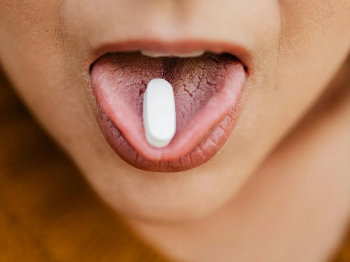 Femeie cu o pastilă pe limbă - Foto: Pexels/kamboopics