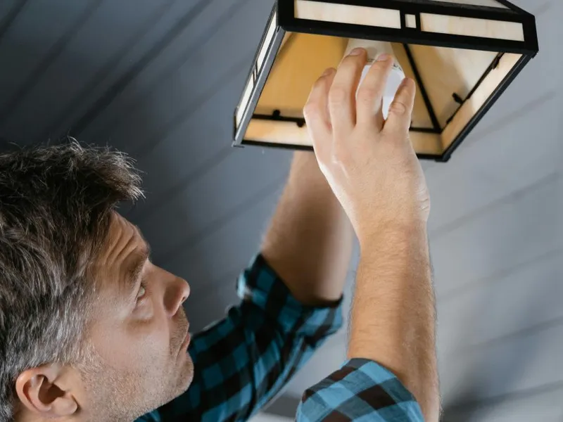 Bărbat punând un bec într-o lustră - Foto: Pexels/MART PRODUCTION