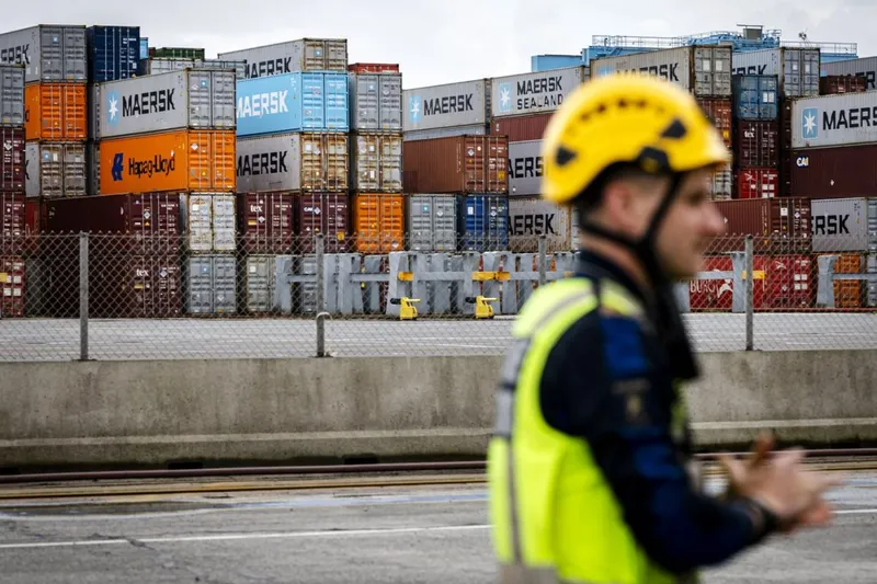Un vameș stă &icirc;n fața unor containere de transport stivuite &icirc;n Portul Rotterdam - Foto: Profimedia Images