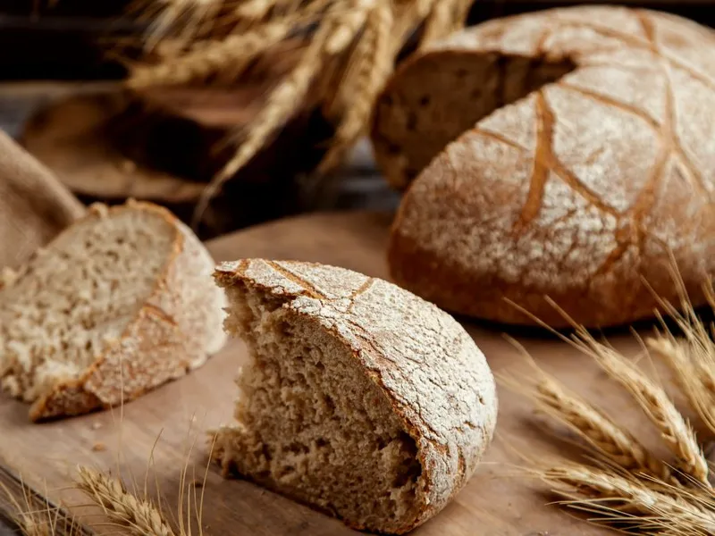 Felie de pâine integrală organică, așezată pe un fund de lemn, în stil rustic - Foto: Freepik/KamranAydinov