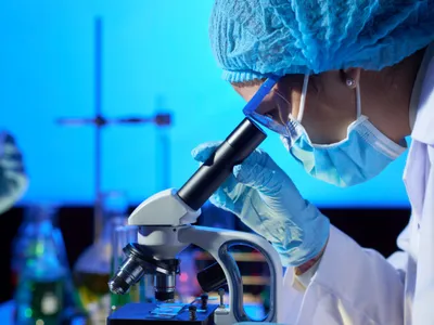 Cercetătoare analizând o probă la microscop - Foto: Magnific.com/pressfoto
