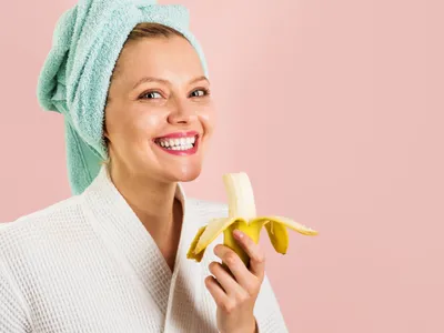 Femeie care zâmbește și ține o banană în mână - Foto: Freepik (rol ilustrativ)