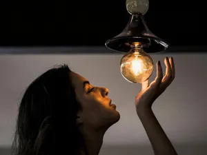 Femeie admirând un bec cu filament - Foto: Pexels/Victor Miyata