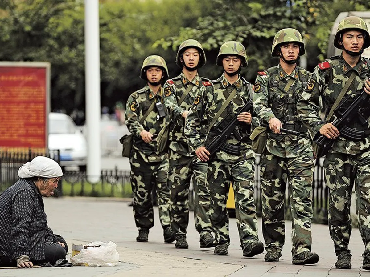 O bătrână musulmană uigură, în capitala regională Urumki, cerșește, în timp ce poliția paramilitară chineză patrulează