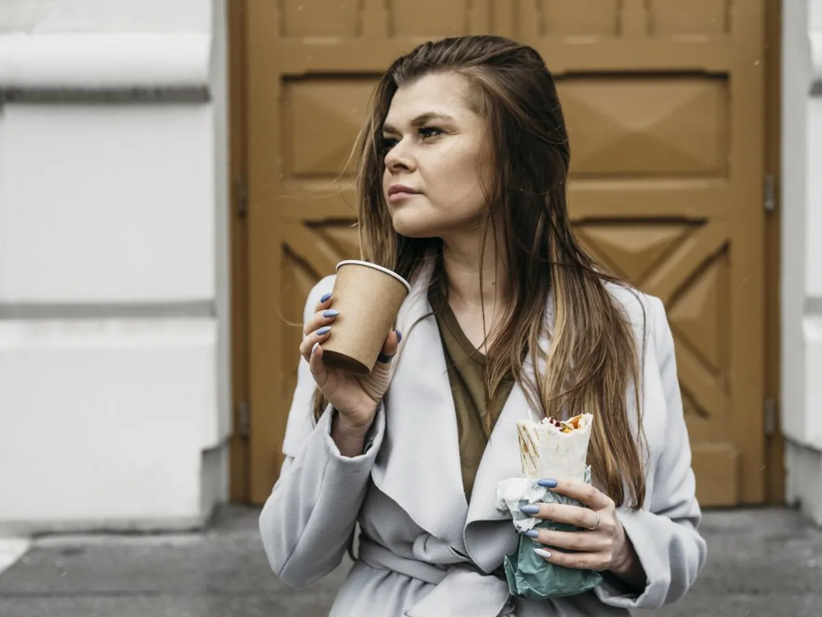 Femeie savurându-şi cafeaua şi uitându-se în lungul străzii - Foto: Magnific.com/freepik