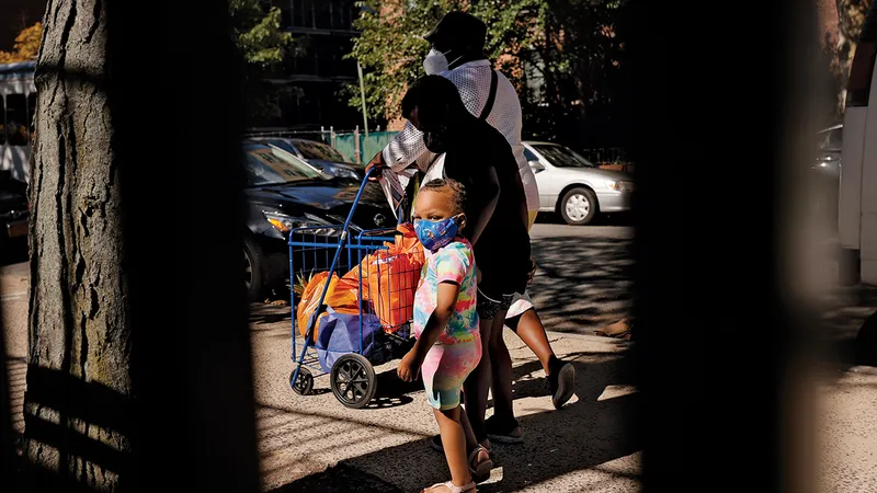DUREREA FOAMEI O femeie și doi copii părăsesc o bancă de alimente din Brooklyn, New York. TEB-ul de vară va oferi familiilor cu venituri mici 120 de dolari de copil pentru cumpărături