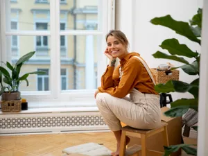 Femeie privind pe geamul apartamentului - Foto: Freepik