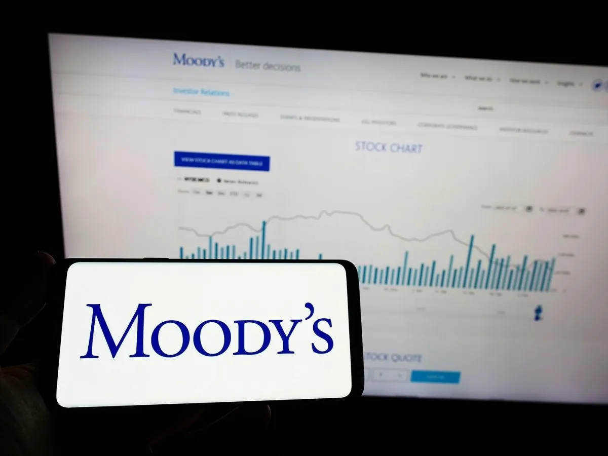 O persoană care ține în mână un telefon mobil cu logo-ul agenției de rating Moody's Investors Service Inc. afișat pe ecran, în fața unei pagini web - Foto: Profimedia Images
