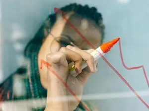 Femeie desenând un grafic, pe un panou transparent - Foto: Pexels/Nataliya Vaitkevich