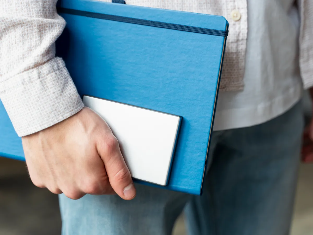 Prim-plan mână ținând SSD și notebook - Foto: Magnific.com (Imagine cu rol ilustrativ)