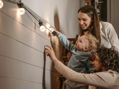 Tânără familie cu copil admirând aranjamentele cu lumini, în afar casei - Foto: Pexels/Pavel Danilyuk