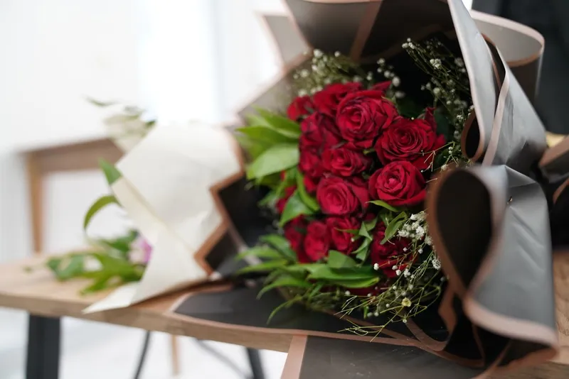Un buchet frumos de trandafiri roșii aranjați elegant cu verdeață pe o masă de lemn - Foto: Pexels (Imagine cu rol ilustrativ)