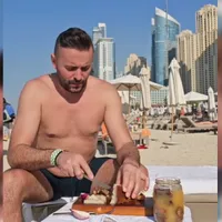 Cuplu de români, cu slănina, ceapa și pălinca pe o plajă din Dubai: În spatele nostru e Burj al-Arab - Foto: Captură Video - Florin Cilica / TikTok