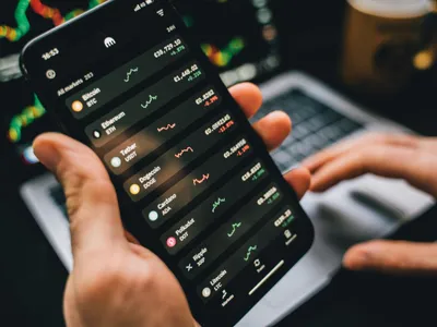 Persoană ţinând în mână un smartphone, pe care se văd listate acţiuni - Foto: Pexels/Alesia Kozik