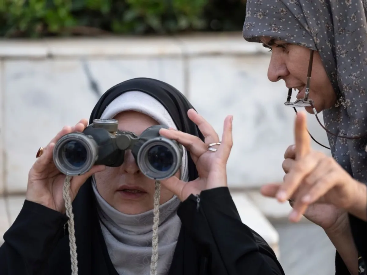 O femeie neidentificată o învaţă cum să folosească binoclul pe o membră a forțelor iraniene de sacrificiu volutar, lângă Teheran - Foto: Profimedia Images