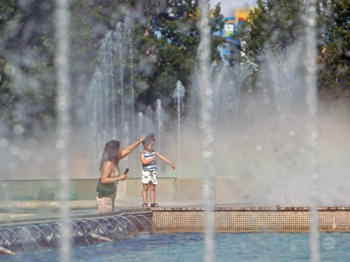 Femeie cu copil pe marginea unei fântâni, în Bucureşti - Foto: Profimedia Images