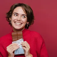 Femeie frumoasă care zâmbește și mănâncă ciocolată - Foto: Freepik